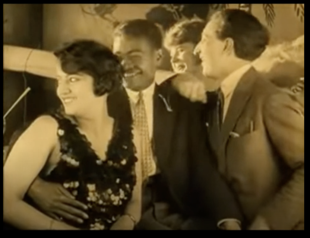 still from "Invitation to a Journey": happy people at a bar ordering drinks, a Black Man and white or light skinned woman embrace as a couple smiling