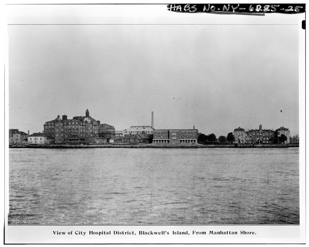 photograph: "View of City Hospital District, Blackwell's Island, From Manhattan Short" - showing the penitentiary, and a smokestack.
