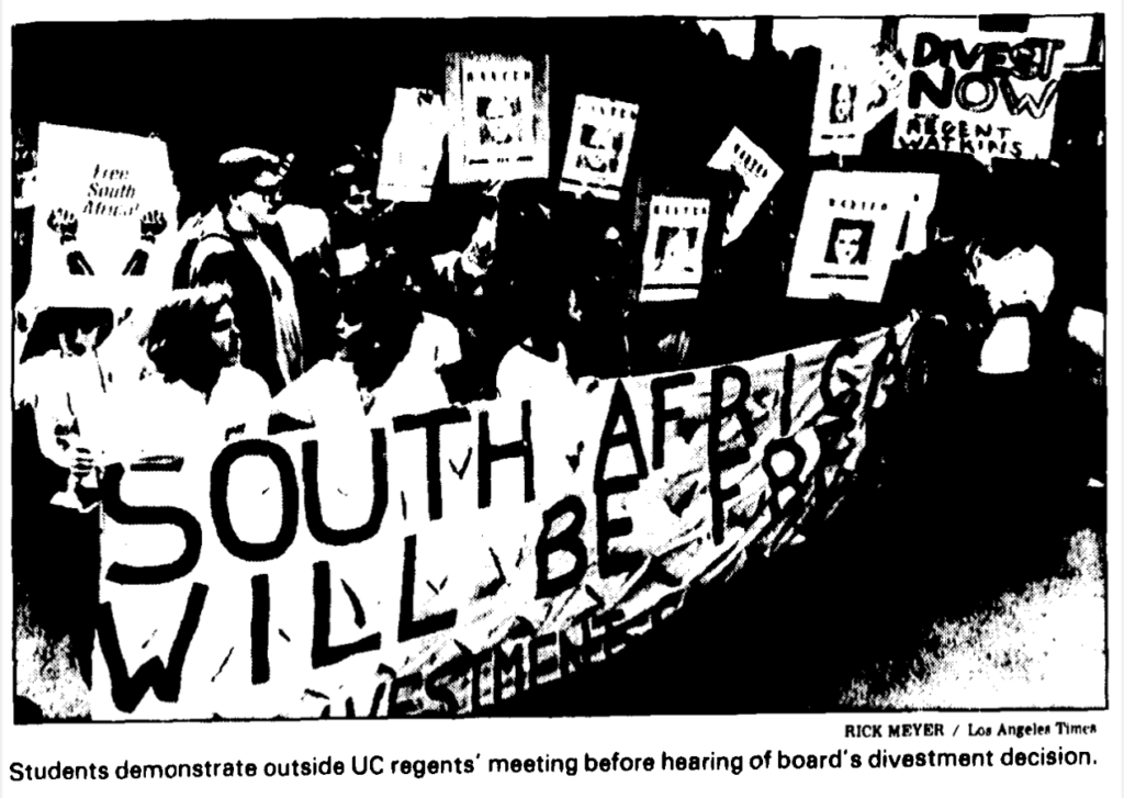 newspaper photograph, students protesting carrying a banner reading "South Africa Will Be Free" - caption: "Students demonstrate outside UC regents' meeting before hearing of board's divestment decision."