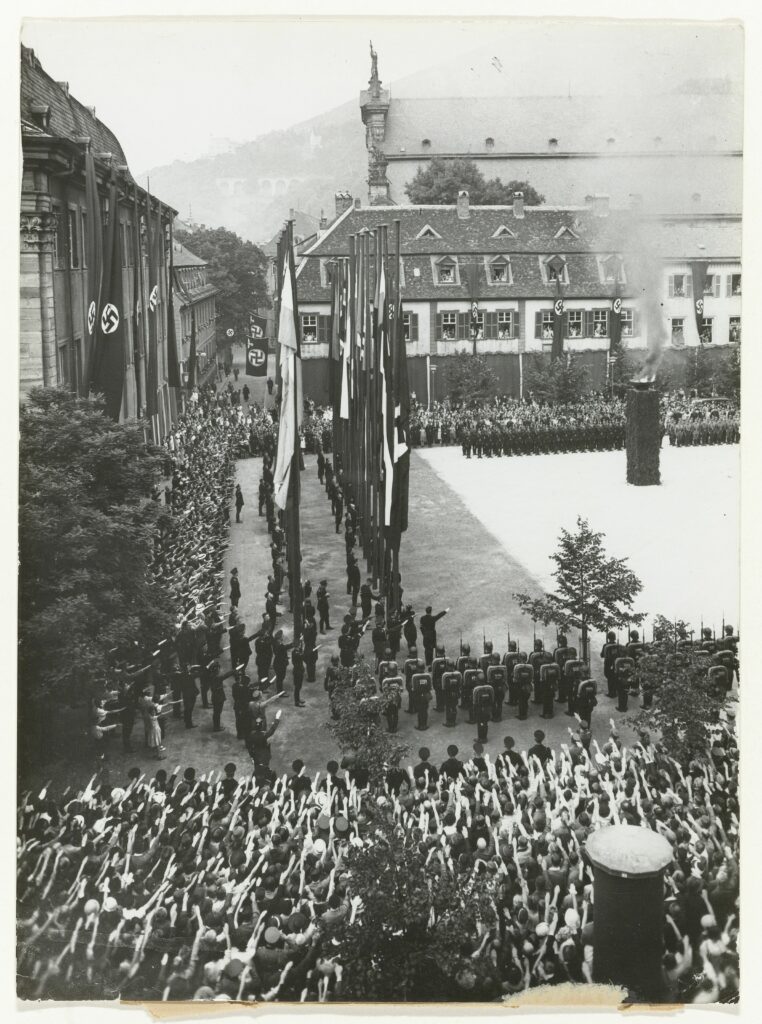 photograph titled "550th Anniversary of Heidelberg University 1936" - huge Nazi flags hang from the buildings, thousands of people doing a Seig Heil.